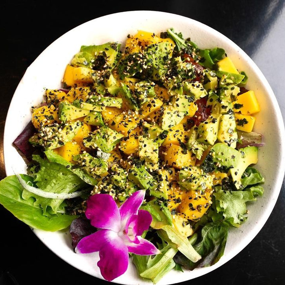 Colorful poke bowl with diced mango, avocado, and sesame seeds, garnished with a purple orchid.