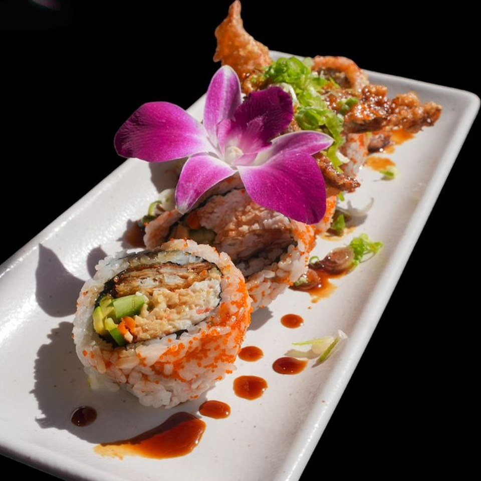 Sushi rolls with orange roe, avocado, and a purple orchid on a white rectangular plate.